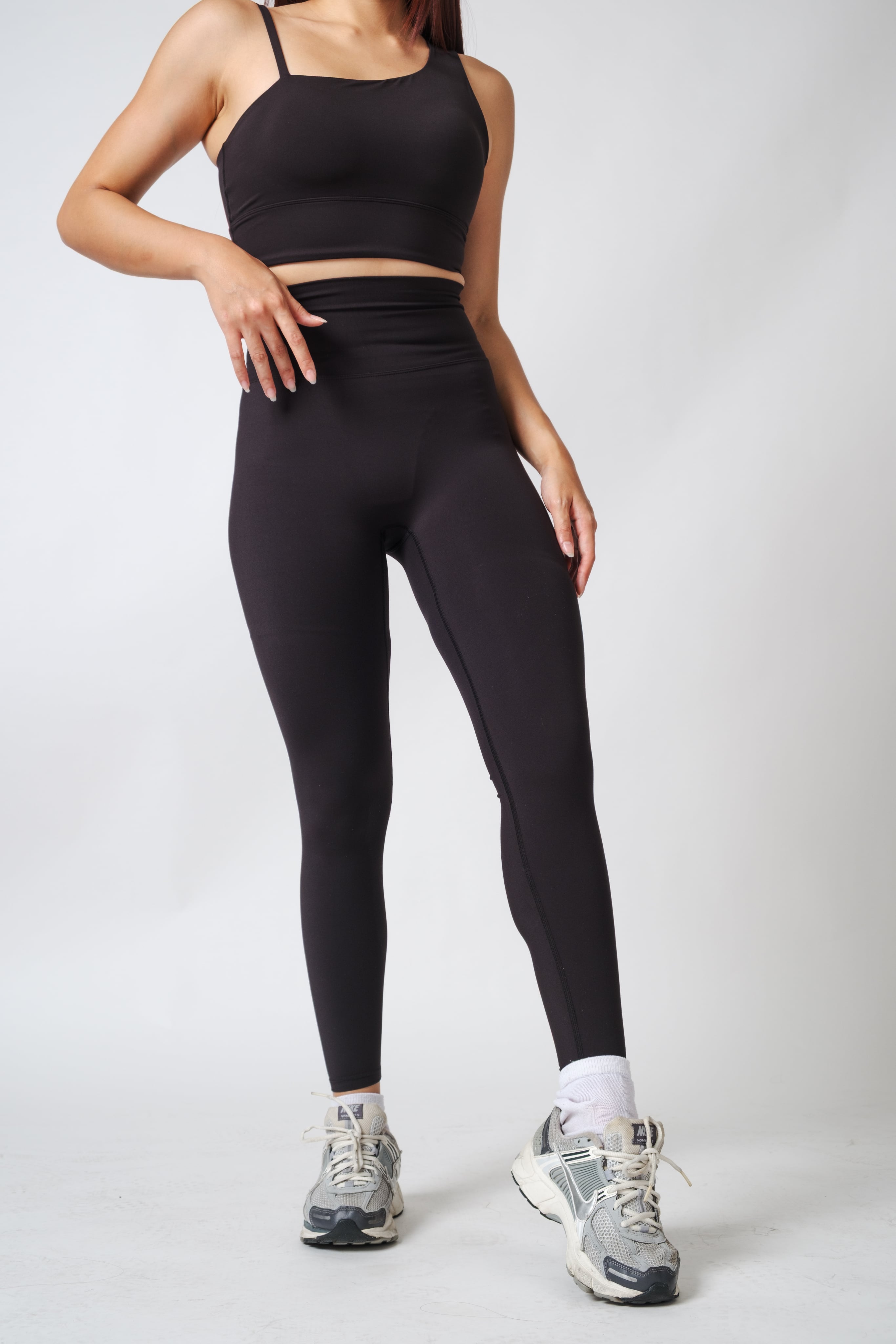 Person wearing black athletic leggings and sports bra on a light gray background